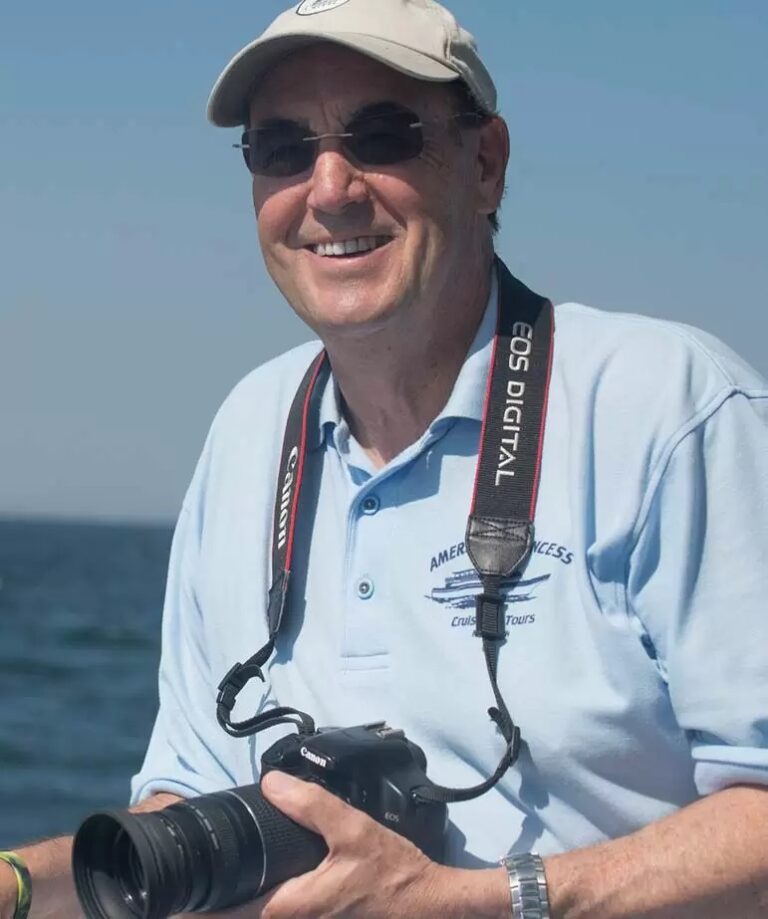 A man smiling while holding a camera on a boat.